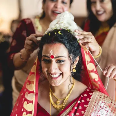 The joy of a Bengali bride. This look features the traditional chandan design on the forehead, a bold red bindi, and classic gold jewelry, capturing the essence of a Bengali wedding.