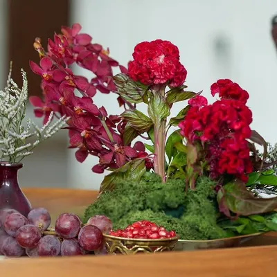 A centerpiece from our 'दाड़म ka Bageecha' theme, featuring a rich palette of red flowers, fresh grapes, and pomegranate seeds in an antique brass bowl. This is where food, art, and nature meet.