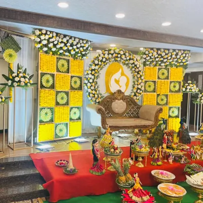 A stunning stage for a traditional baby shower, or Seemantha. The backdrop features intricate panels of yellow and white flowers with a central silhouette of a mother and child, creating a meaningful and beautiful setting.
