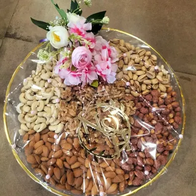 A classic dry fruit platter featuring an assortment of almonds, cashews, walnuts, and pistachios. The arrangement is finished with a custom acrylic monogram and a small floral bouquet, making it an elegant and healthy gift option.