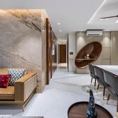An overview of the living and dining area in The Filigree House. A feature wall of book-matched marble, rich wood paneling, and a unique, sculptural shelving unit create a space that is both luxurious and inviting.