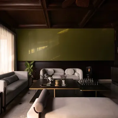 A wide view of the formal living area, where I balanced the dark, coffered teak ceiling with light grey sofas and an olive accent wall. The design creates a sophisticated space for conversation, grounded in traditional architectural elements.