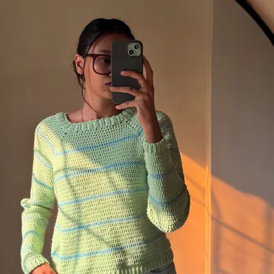 A mirror selfie in the pastel striped sweater. It has a classic crew neck and a relaxed fit that's super comfortable.