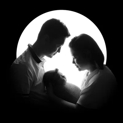 An artistic silhouette of parents admiring their newborn, creating a dramatic and timeless family portrait. This style focuses on the outlines and the emotional connection within the family.