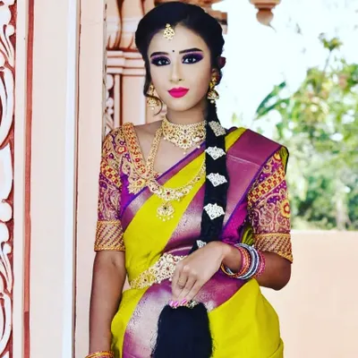 A full-length view of a traditional South Indian bridal style. The look features a classic long braid, a vibrant Kanjivaram saree, and makeup with a bold lip and defined eyes that tie the entire look together.
