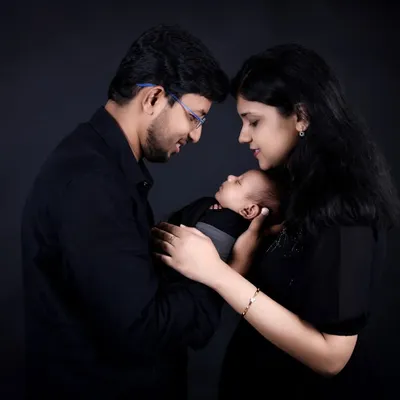 An intimate family moment captured in our classic studio style. The parents gaze lovingly at their newborn, their faces close together, creating a powerful image of connection against a simple black background.
