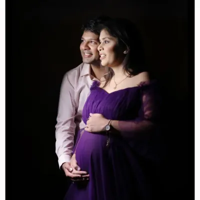A classic low-key studio portrait of a couple. The lighting creates a warm, intimate mood, focusing on their happy expressions as they await their baby.