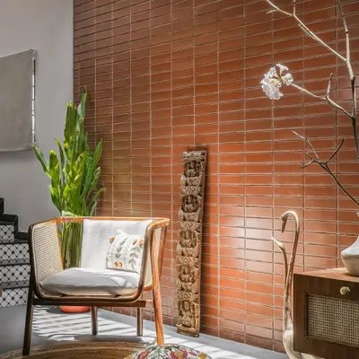 An exposed brick wall, made from local 'ittige', serves as a warm, textured backdrop for a contemporary cane armchair and traditional Indian artifacts in this cozy reading nook.