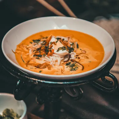 A beautifully presented bowl of Khow Suey, a Burmese noodle soup, showcasing our Pan-Asian expertise.