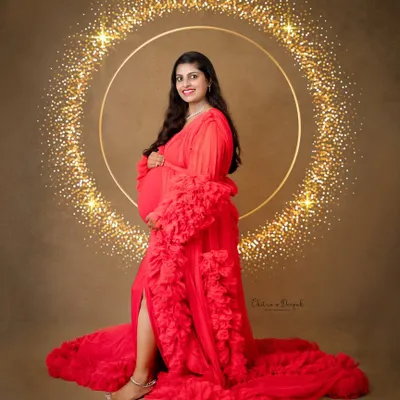 A vision in red. This mom-to-be is glowing in one of our signature ruffled gowns, set against a sparkling gold halo backdrop for a touch of high-end glamour.