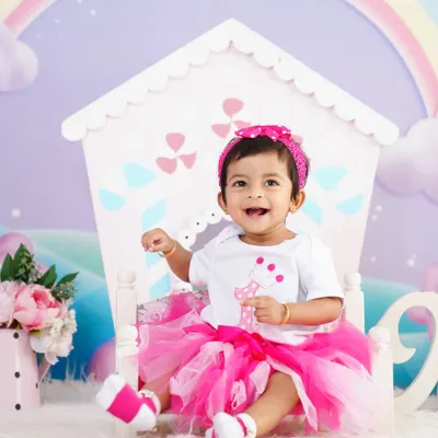 A joyful first birthday shoot! This little girl is shining in her pink tutu, sitting in front of a cute dollhouse prop with a rainbow background.