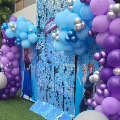 A close-up of our shimmering Frozen theme backdrop. The sequin wall and character cutouts of Elsa and Anna, framed by blue and purple balloons, create a magical icy palace.