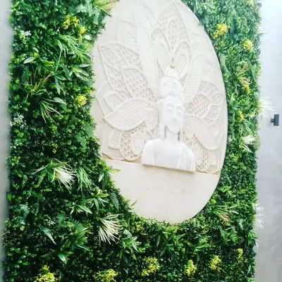 I can integrate art and sculptures into my green walls. This design features a custom-carved Buddha statue set within a circle, surrounded by a lush artificial vertical garden.