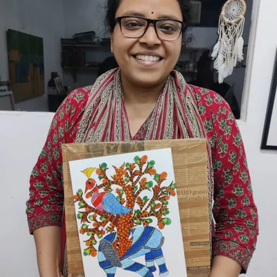 A student proudly holds her completed Gond painting of an elephant, showcasing the distinctive patterns and vibrant colors of this traditional tribal art form.