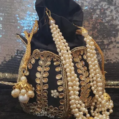 This black velvet potli bag is pure elegance. It features delicate gold-tone leaf embroidery and a beautiful pearl strap, making it a sophisticated accessory for an evening event or wedding reception.