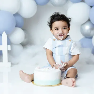 A messy and happy moment from a first birthday cakesmash. This little boy is enjoying his first taste of cake in our blue and white balloon setup.