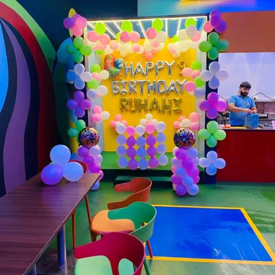 A colorful birthday setup in a cafe for Ruhani's 9th birthday. The decor features a bright yellow backdrop with a pastel balloon garland and "Happy Birthday" foil letters.