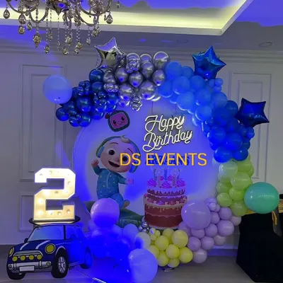 A vibrant Cocomelon birthday setup perfect for a second birthday. This decoration features a circular backdrop with the main character, a colorful balloon garland, a light-up marquee number "2", and a bright neon sign.