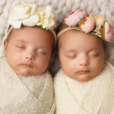 Two peas in a pod. These twin newborn girls are swaddled and sleeping side-by-side, each wearing a beautiful floral headband.