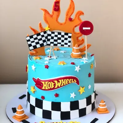 A fiery Hot Wheels cake for a fifth birthday, complete with a racetrack border, checkered flags, and traffic cones.