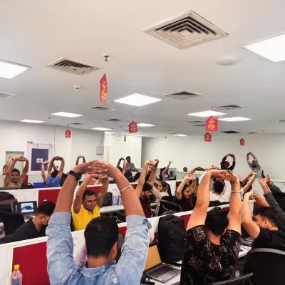 A full team engaged in a synchronized desk stretch. This simple overhead arm stretch helps to open up the shoulders and lengthen the spine, providing immediate relief from the strain of sitting at a computer.