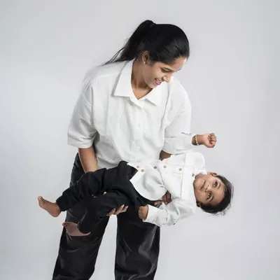 A mother holds her baby boy, their matching white shirts creating a clean and simple look. The playful tilt and their smiles capture a moment of pure, uncomplicated joy.