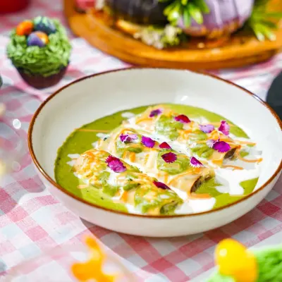 A vibrant bowl of green curry with cannelloni, garnished with edible flowers, as part of a whimsical Easter brunch. The bright, festive setting enhances the dish's appeal.