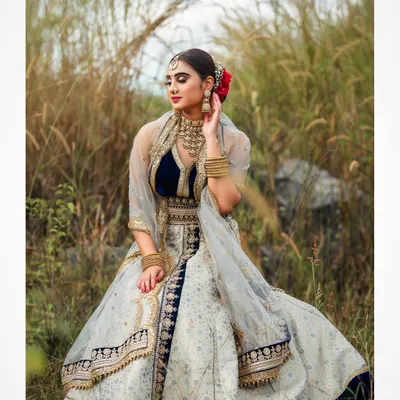 An outdoor bridal shoot capturing a serene and elegant moment. The natural setting complements the traditional lehenga, and the soft lighting highlights the delicate details of the fabric and embroidery.