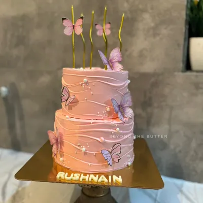 A beautiful two-tier butterfly themed cake. The soft pink buttercream has a gentle wave texture, adorned with delicate butterflies and pearl sprinkles, making it perfect for a special birthday.