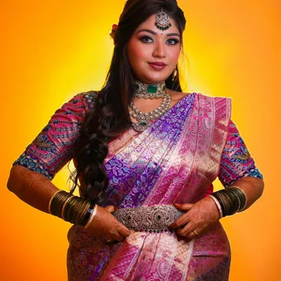 A stunning bridal portrait against a vibrant yellow backdrop. The rich colors of her saree and jewelry create a powerful and beautiful image.