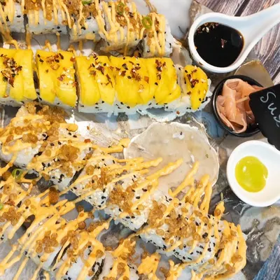 An overhead view of our assorted sushi platter. We offer a wide variety of rolls, including tempura, classic maki, and uramaki, all drizzled with delicious sauces and served with wasabi and soy.