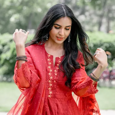 A candid moment from a pre-wedding shoot. The bride-to-be is in a beautiful red dress, captured in a natural, unposed moment in a lovely garden setting.