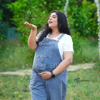A fun and whimsical outdoor shot. The mother-to-be, dressed in cute denim overalls, blows bubbles in our garden.