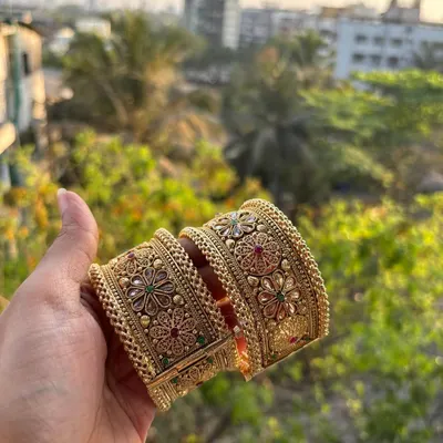 A pair of our premium collection bangles, held up against the light. These broad kadas feature intricate floral designs with red and green stones.
