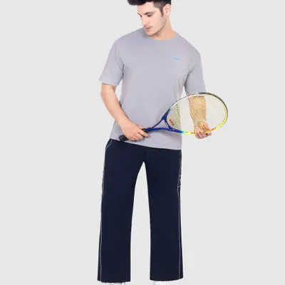 A full length e-commerce model shot for a sportswear brand. The clean grey background ensures no distractions, keeping the focus entirely on the fit and style of the t-shirt and track pants.