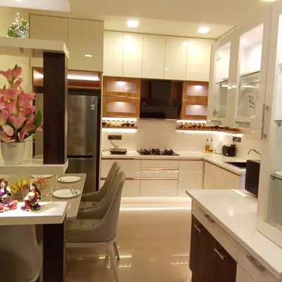 This L-shaped modular kitchen is designed for both beauty and function. The combination of off-white and wood-finish cabinets, frosted glass shutters, and under-cabinet lighting creates a warm, inviting space for cooking and gathering, complete with a cozy breakfast counter.