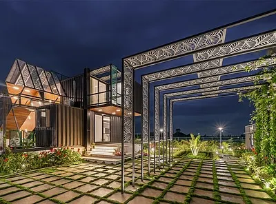 The QBINN TUSKER container home illuminated at night, with a vine-covered pergola creating a dramatic, glowing entryway. This shot captures the project's innovative use of industrial materials and landscape integration.