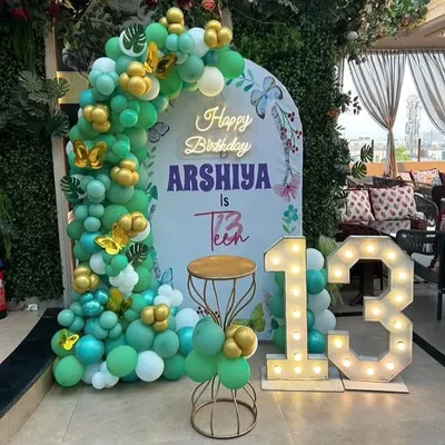A beautiful butterfly theme for a 13th birthday. This outdoor setup features a teal and gold balloon arch, a personalized backdrop, and large light-up numbers for the big teen birthday.