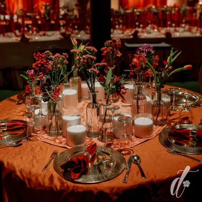 The tables were set with deep orange linens, hammered metal charger plates, and rich red napkins. Centerpieces of red flowers in clear glass vases, surrounded by candles, created an intimate and warm dining setting.