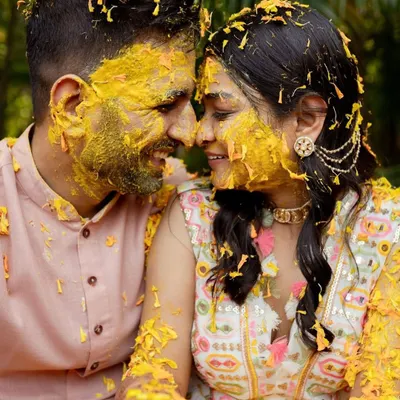 A candid, joyful moment from a Haldi ceremony, with the couple sharing a laugh, covered in turmeric and flower petals. This photo is all about capturing the raw, uninhibited fun of pre-wedding festivities.