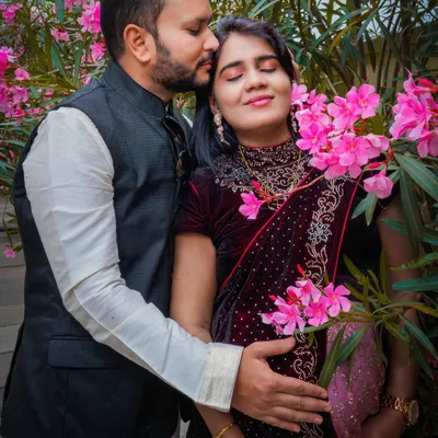 An intimate moment captured amidst blooming flowers. The partner's gentle kiss and their hands cradling the baby bump create a portrait filled with warmth and affection.