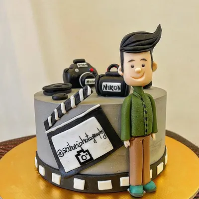 The perfect cake for a photographer! This design features a hand-sculpted fondant caricature, a miniature Nikon camera, a clapperboard, and a film strip border, celebrating a passion for capturing memories.