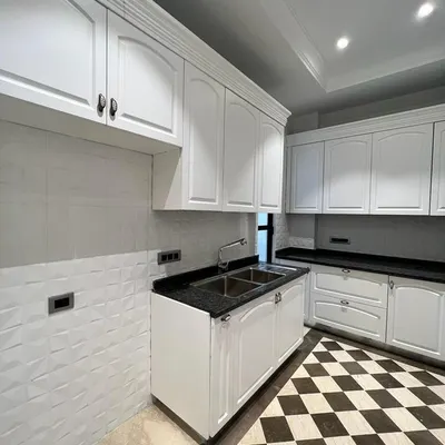 A full view of our classic white kitchen. It features ample storage with PU-finished cabinets, a dark granite countertop, and our signature checkerboard marble flooring.