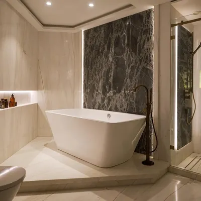 A master bathroom from our 'Urban Tranquility' project. The freestanding tub is the star, set against a dramatic dark marble accent wall. Warm, indirect lighting and light marble on the surrounding walls create a chic, spa-like atmosphere.