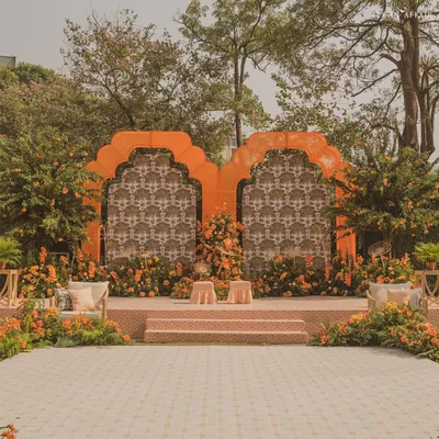 The main stage for our 'Orange Orchard' Haldi ceremony, featuring a backdrop of custom-printed fabric framed by vibrant orange arches and surrounded by orange trees.