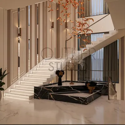 The base of this staircase is a sculptural platform made of black marble, serving as both a functional step and an art installation. A cascading metallic light fixture hangs above, drawing the eye upward.