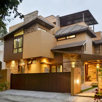 The 'Mountain Abode' at dusk, where architectural form meets natural texture. The combination of stacked stone, warm ochre walls, and metal roofing creates a distinctive modern rustic aesthetic.