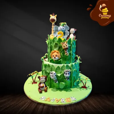 This two-tier jungle cake is covered in lush green fondant leaves. It features adorable animals like a giraffe, elephant, lion, and monkeys peeking out, creating a fun safari adventure for a second birthday.
