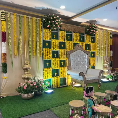 A beautiful stage setup for a traditional ceremony, featuring a backdrop of marigolds, hanging flower garlands, and an ornate white chair for the guest of honor.