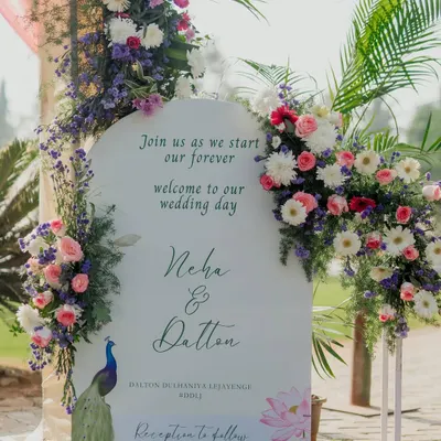 A beautiful welcome sign for a wedding, designed in a modern arch shape with elegant calligraphy. We adorned it with lush arrangements of pastel flowers and a peacock illustration to add a touch of Indian royalty.